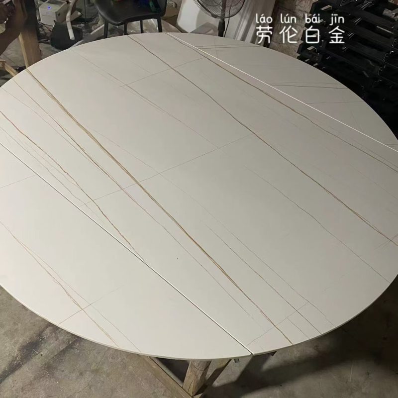 工場內一張啞光勞倫白金岩板圓餐枱枱面，米白底配幼長金啡色石紋，分件接縫清楚可見，枱面放在木架上待安裝。