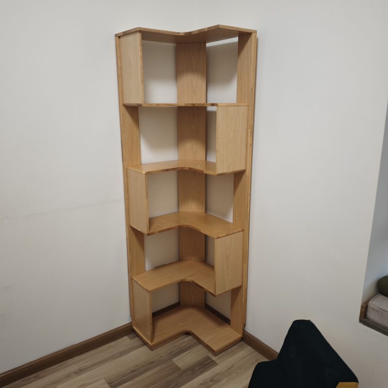 淺原木色Peyton落地儲物書架擺放喺白牆牆角，深啡色木地板，右下角有塊深色地毯同綠色圓型咕臣，5層階梯式錯位開放層板暫時無擺嘢，露出木紋接駁位。