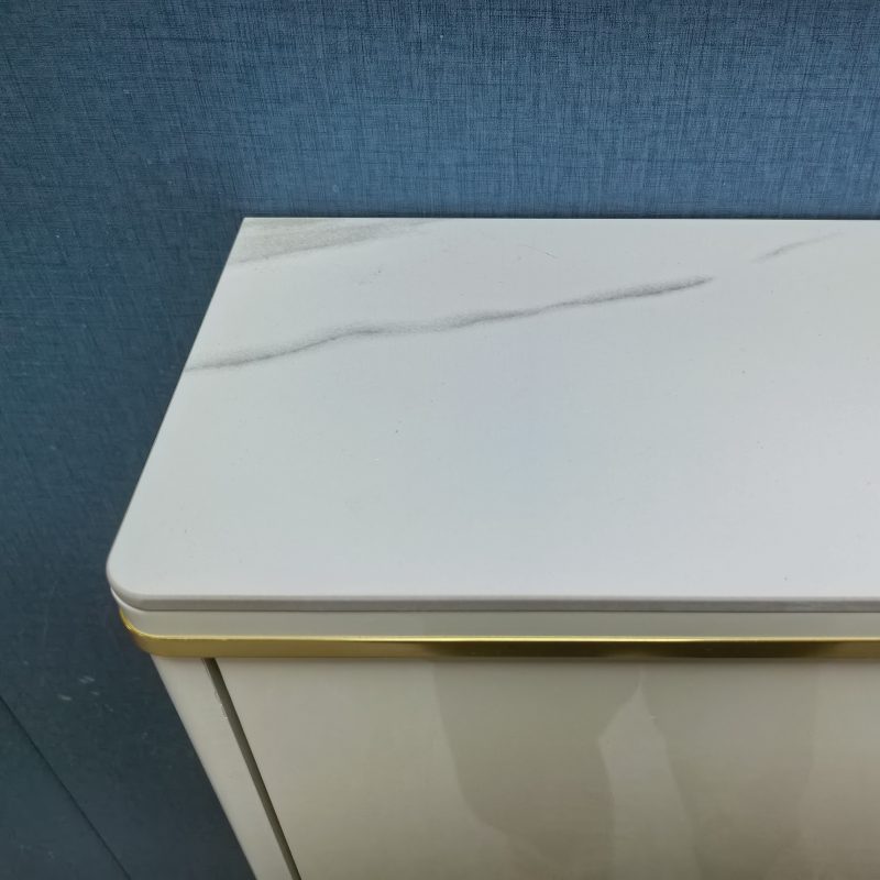 Caleb超薄鞋櫃頂部岩板枱面近距離特寫，白色底配灰色雲石紋路，邊位用金色金屬收邊條包住，亮光米白櫃身反光，背景係深藍布紋牆。