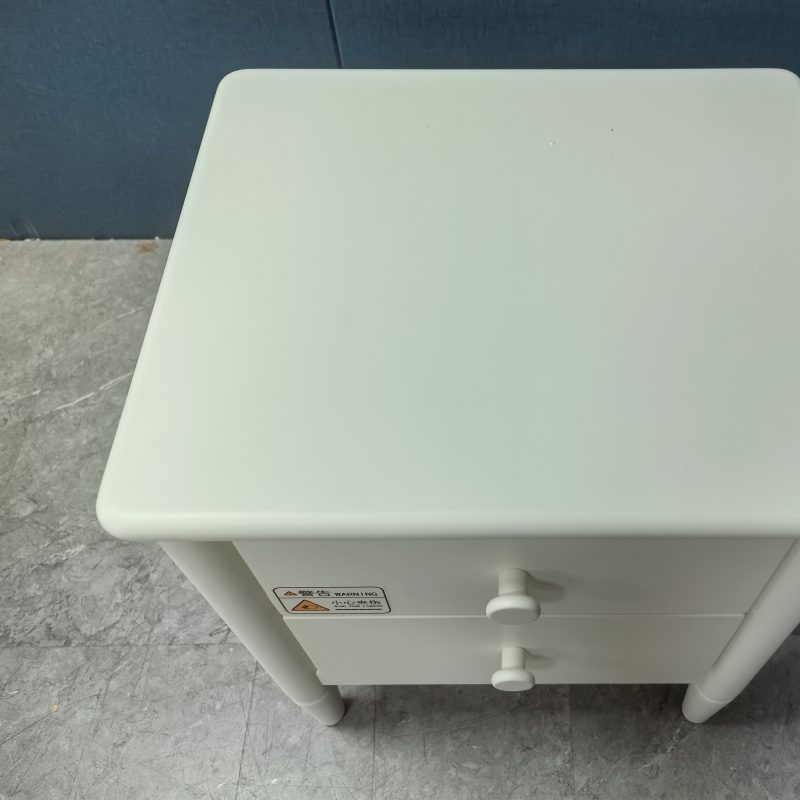由高處俯視床頭櫃頂面，方正桌面奶油白啞光反射柔和光線，四角圓角修飾，前方可見兩個白色圓形拉手位置，深藍牆板同大理石灰地面襯托，整體乾淨無雜物。