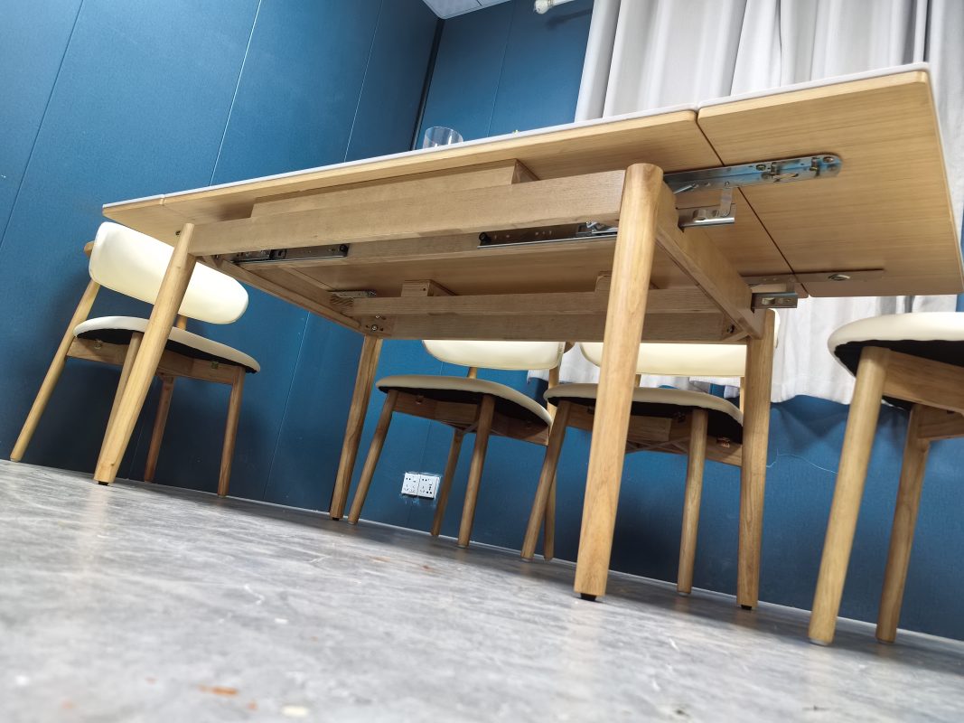 斜向低角度拍攝拉開中的Reese伸縮餐枱，右側雪山白岩板延伸板向外移出，金屬滑軌、扣件及原木色實木承托架完整可見。