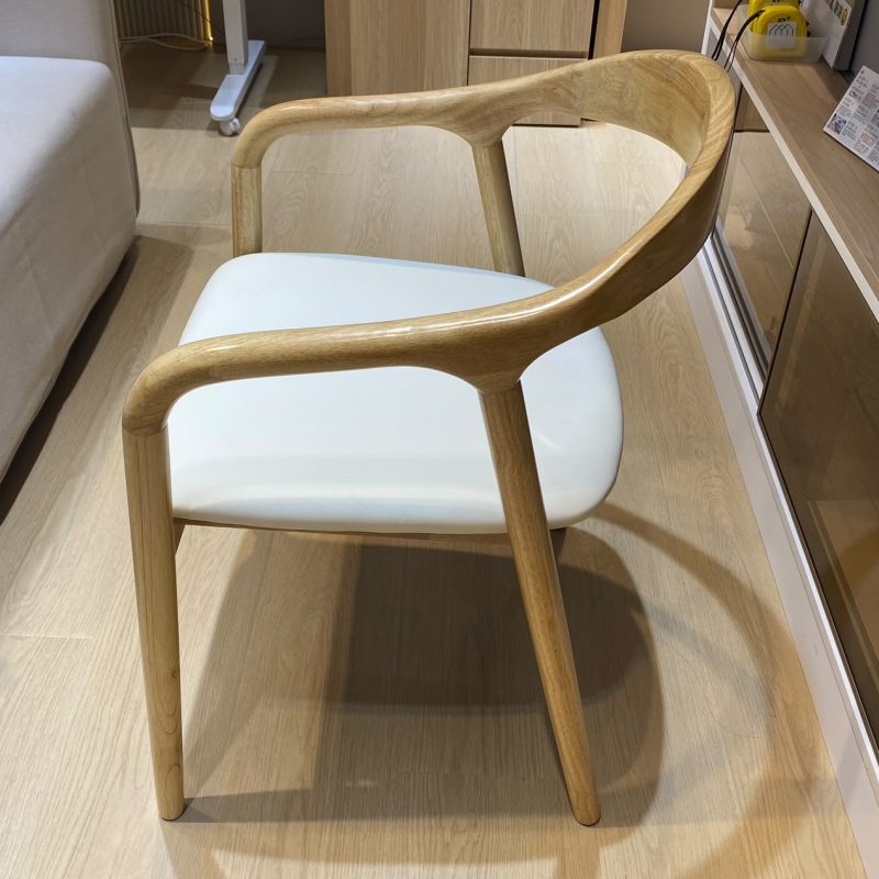 側前方拍攝一張舒美特實木扶手餐椅，淺木色弧形靠背沿兩側延伸至扶手，四支幼身椅腳略向外張，座框內配米白色厚身軟墊。