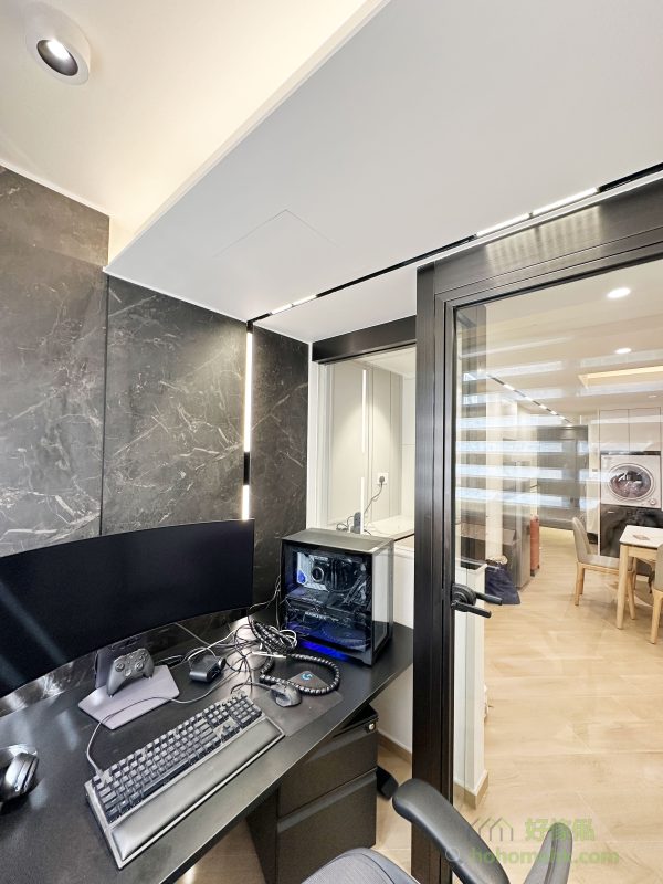 書房的牆身採用了黑色石紋護牆板，與簡約的書桌和高性能電腦設備相得益彰，營造出專業且時尚的工作環境。玻璃間隔的設計既保留了客廳的自然採光，又讓書房保持一定的私密性，實現了美感與功能的平衡。