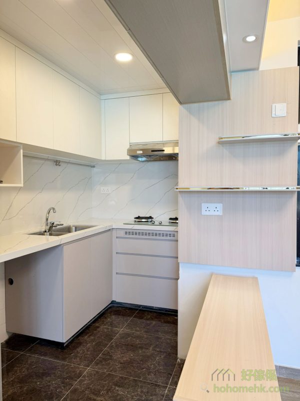 廚櫃、浴室櫃及客廳、睡房的訂造傢俬均採用相同的材質及設計風格，令整個單位的視覺效果顯得更為統一。無論是廚房的潔白牆身，還是浴室的簡約線條，每一件訂造傢俬都體現了細緻的工藝。開放式廚房選擇灰杏色和大面積的奶油色，使整個客廳空間顯得更寬敞光亮。