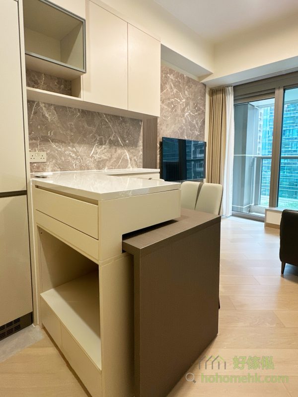 廳櫃與吧枱的設計不僅是廚房與客廳的分隔，更能透過石面枱面的延伸大幅增加廚櫃的工作枱面。特別是錯層的創新設計，讓餐枱藏於吧枱之下，需要時可拉出變成獨立餐枱，節省空間之餘，亦讓中島更具層次感與特色，滿足現代家庭對靈活性的需求。