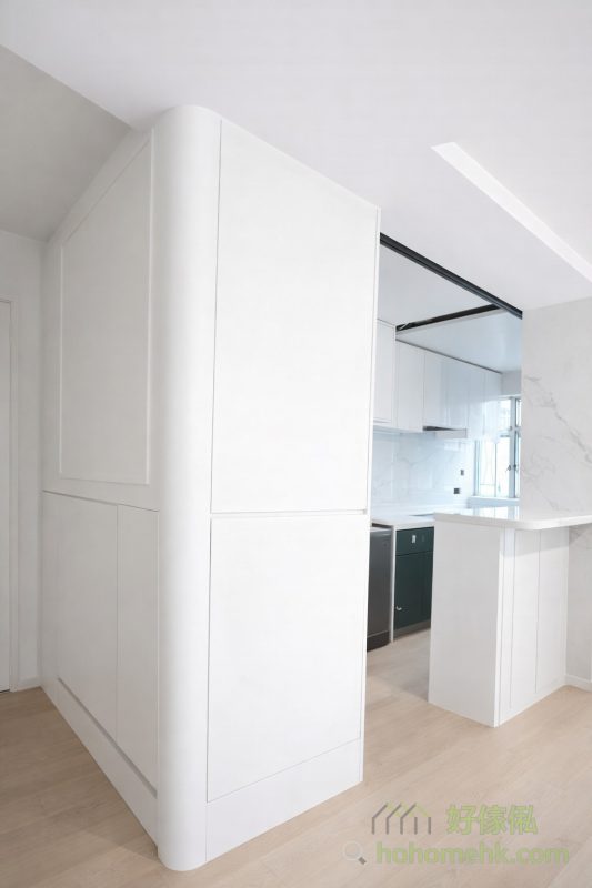 在廚房與玄關之間，設置了一個工人床櫃作分隔，既能為工人姐姐提供舒適的休息空間，又能節省牆磚的建築成本，充分利用每一吋空間。這樣的設計實用而靈活，完美契合香港家庭的需求。純白選色也是呼應了廚房和客廳的傢俬風格。
