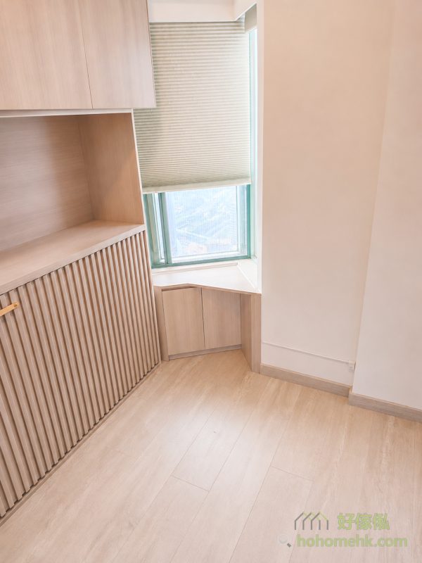 客房窗邊的三角角位設有淺木紋兩門矮櫃，上方接白色窗台，左側為直條子側翻床櫃，中央鋪設淺色木紋地板並留出走動位置。